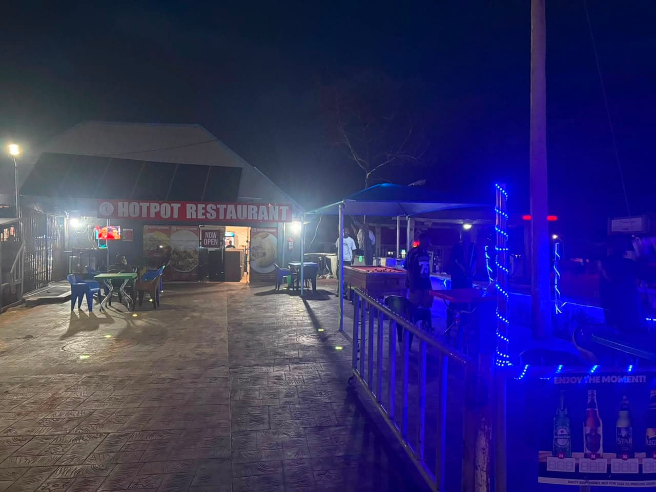 The restaurant at night with the sign board lit and lights along the outdoor seating