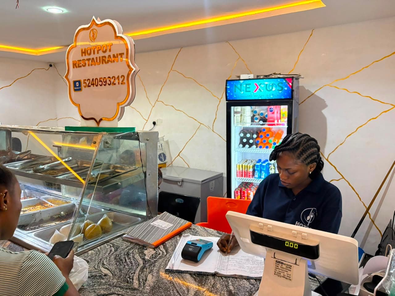 Staff at the order counter beside the food display and the drinks fridge